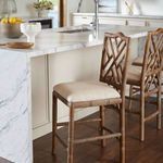 Close side view of two grey coastal counter stools placed at a marble kitchen island on dark wood floor