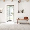 Bellamy Sky Rug shown in a wider room view with a copper chair, wooden bench with accessories, and open door to outside