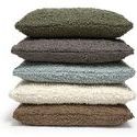 Stack of five bouclé pillows in various colors including olive, charcoal, blue-gray, cream, and brown