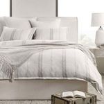 Duvet styled on bed with fringed throw and matching striped pillows in a neutral bedroom setting