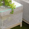 Outdoor side table next to woven outdoor sofa armrest with lantern and greenery on glass surface
