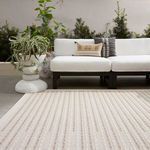 View of rug outside with lush green plants and sculptural white planter beside sofa