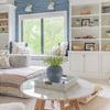 Tray placed on round marble coffee table in bright living room with shelves and windows