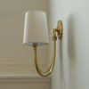 Single sconce side view showing curved arm and round backplate shadow on beige wall