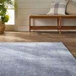 Light blue rug covering floor in room with wood flooring, bench, and pillow in background