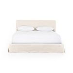 Close-up of cream linen slipcovered headboard and white bedding corner