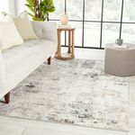 Jehan rug styled in a light-filled living room under sofa and ottoman with natural wood side table and green plant