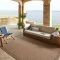 Merrick Natural rug styled outdoors on patio beneath wicker sofa with lake view in background