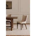 Posta dining chair beside wooden dining table in neutral-toned room with beige rug and framed art
