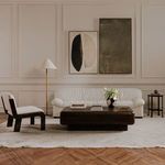 Modern living room scene with chair beside sofa, coffee table, floor lamp, and framed art on wall