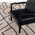 Black leather chair legs on textured outdoor shag rug with geometric black line pattern