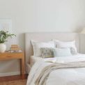Throw layered on bed with headboard and wood bedside table with books and plant