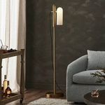 Lamp lit in dark room setting between gray boucle sofa and wooden cart with bottles