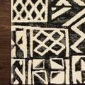 Close-up showing corner edge and textured weave details of the ivory and black geometric rug on wood floor