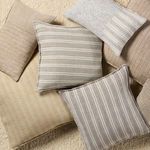 Lucien cream and gray striped pillow among assorted earthy-toned pillows on textured carpet