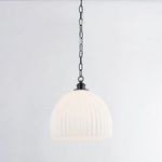 Pendant light illuminated showing warm soft glow through fluted glass shade hanging from chain