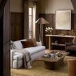 Room setting with lamp near white sofa, wooden walls, and beige window curtains