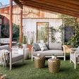 Mud cloth print pillows on light gray outdoor seating under wooden pergola with plants