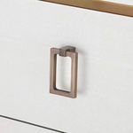Rectangular brass drawer pull close-up on textured white lacquered linen drawer