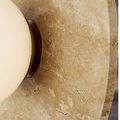 Close-up of travertine disc showing detailed stone texture and antique brass hardware behind frosted globe