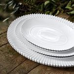 Three nested ceramic platters on rustic wood table with greenery background, showing scale and styling