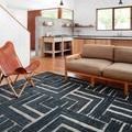 Rug shown in a modern living room with tan sofa and leather chair on polished wood floor
