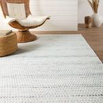 Rug partially under wicker chair and round woven ottoman on wood floor near white shiplap wall