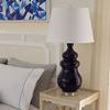 Closer side view of Maila Lamp showing the white drum shade and ceramic base near bedsheet and pillows