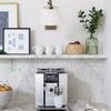 Single bamboo basket holding red apples, styled on kitchen shelf beside green glass vase and coffee setup
