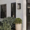 Royster Outdoor Wall Sconce installed next to black window on white brick facade with potted greenery