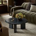 Round black marble coffee table styled in intimate living room with dark green sofa and decorative pillows