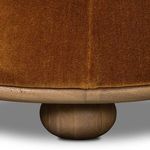 Close-up of wooden base and one rounded leg with rich walnut finish beneath rust upholstery