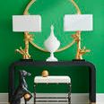 Front view of console table styled with gold coral lamps, white urn, green wall, and decorative stool