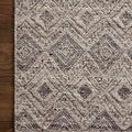 Close-up showing detailed woven diamond pattern and edge of taupe and grey geometric rug on wood floor