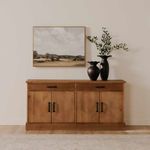 Styled in a room setting against a beige wall with a framed landscape painting and two black vases on top