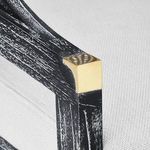 Detail of brass corner cap on the top of the chair armrest against black wood