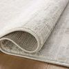Close-up of rug folded back to reveal woven backing and pile texture on hardwood floor.