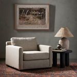Chair styled in a living room with dark table, lamp, and artwork above on textured gray wall