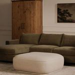 Marion Square Ottoman placed in a living room in front of green sectional sofa and wooden cabinet