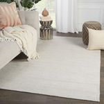 Low-profile solid ivory and light gray rug styled in modern living room with gray sofa and wooden floor