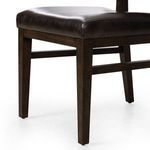 Close-up showing corner of padded leather seat and oak chair leg with visible wood grain texture