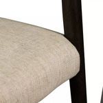Close-up detail of front left corner of padded seat and carbon-finished chair leg with wood grain