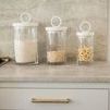 Three Bianca canisters filled with grains and pasta arranged on marble kitchen countertop near stove