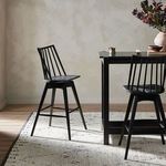 Lewis Swivel Stool shown in a dining room setting with table and rug, angled view
