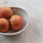 Top angled view showing three grapefruits inside the colander on textured surface