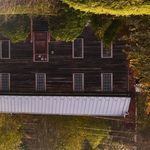 Close-up of rustic dark wood house facade with windows and white metal roof reflected in pond