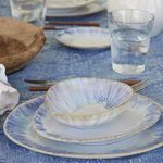 Shallow bowl styled on matching plates on blue textured tablecloth with glass of water and wooden utensils