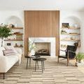 Rug styled in a living room with sofa, armchair, black nesting tables, and fireplace