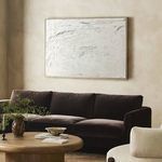 Modern living space showing cream-based painting above dark sofa, complemented by green leafy plant and minimalistic decor