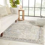 Rug styled in a bright living room next to a beige sofa, round wooden side table, and pouf